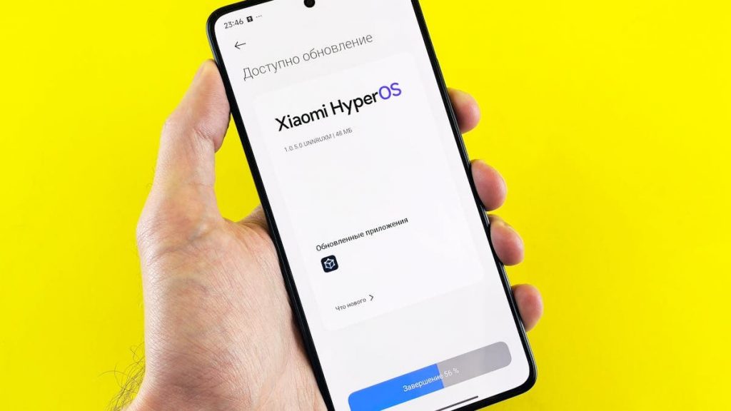 Hand holding smartphone showing Xiaomi HyperOS update screen on yellow background.
