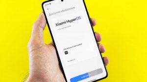 Hand holding smartphone showing Xiaomi HyperOS update screen on yellow background.